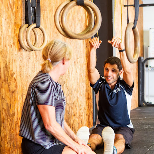 A physio guiding a patient through a shoulder mobility exercise using gymnastic rings in the clinic